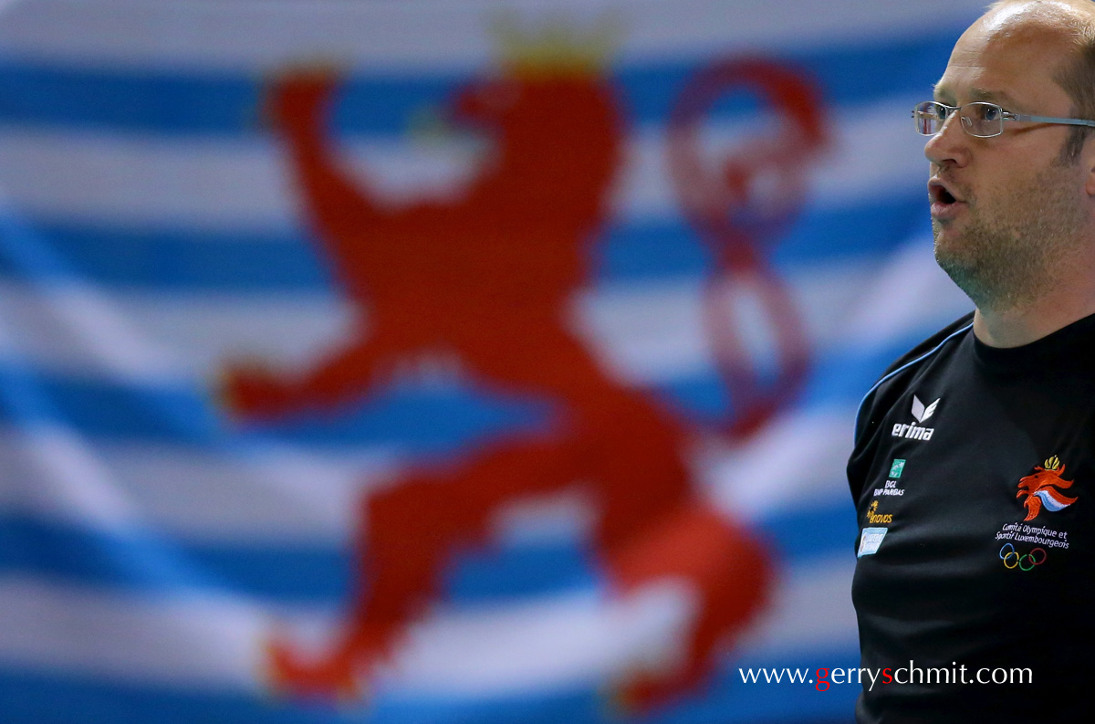 Burkard DISCH (national Coach of Volleyball Luxembourg) stands in front of the Flag 'Roude Leiw' 